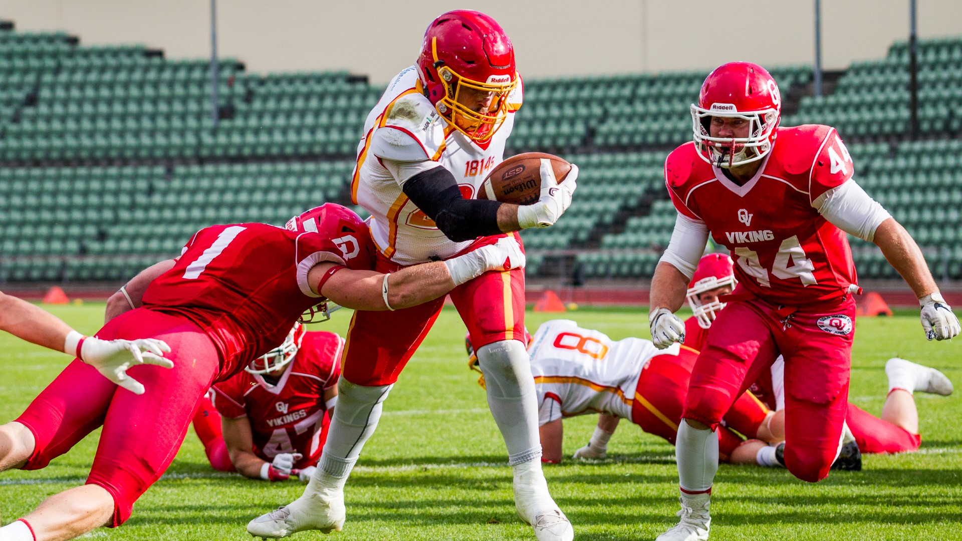 Flere utøvere i amerikansk fotball i en kamp på gresset. En løper med ballen, mens flere kaster seg etter for å takle.